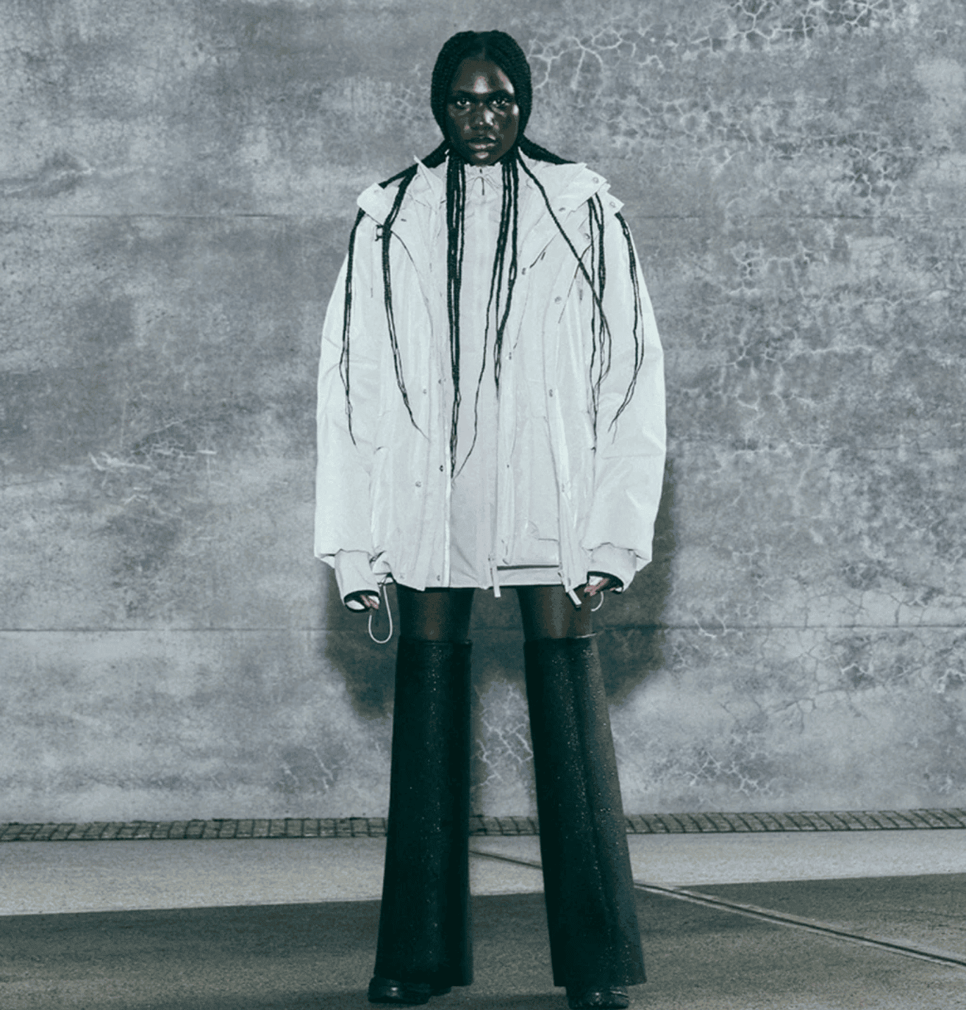 Sleek fashion model wearing oversized white jacket with black high boots for urban streetwear.