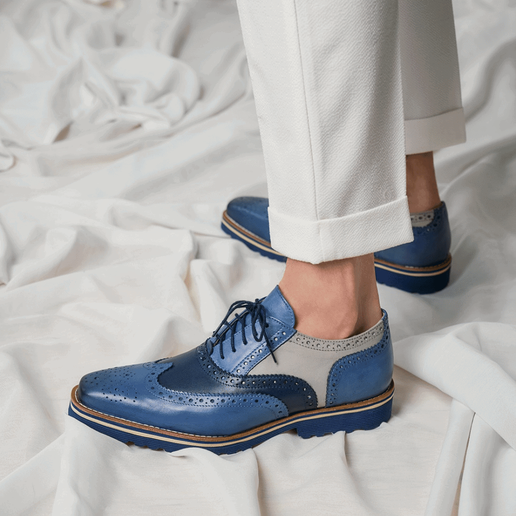 Blue brogue shoes with white pants on a white fabric background.