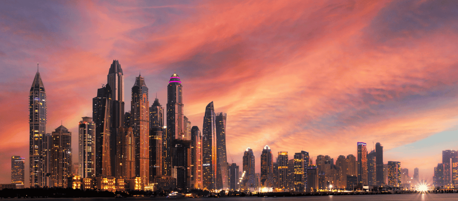 Vibrant Dubai skyline at sunset with illuminated skyscrapers and colorful sky.