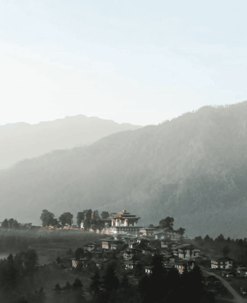 Mountain landscape with traditional architecture and lush greenery, scenic view of Dzong-style building in Bhutan, peaceful rural scene, lush hills and clouds in background.