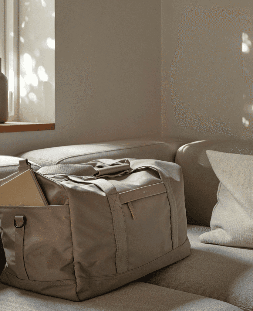 Duffel bag on beige sofa with sunlight and shadows, cozy and minimalist aesthetic.