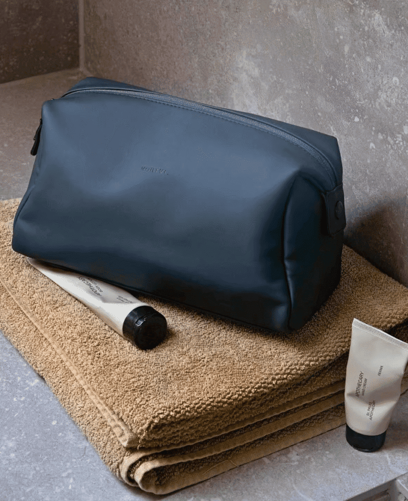 NORTVI toiletry bag with skincare products on beige towels in bathroom setting.