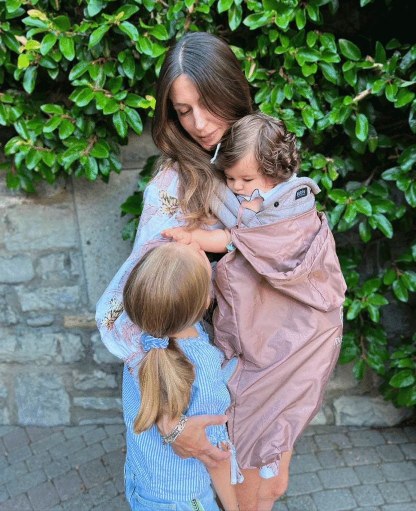Bushes with green leaves, woman hugging children, outdoor natural scene.