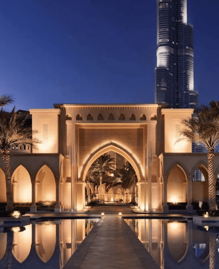 Luxurious hotel entrance with modern architecture and warm lighting, Dubai cityscape in background.