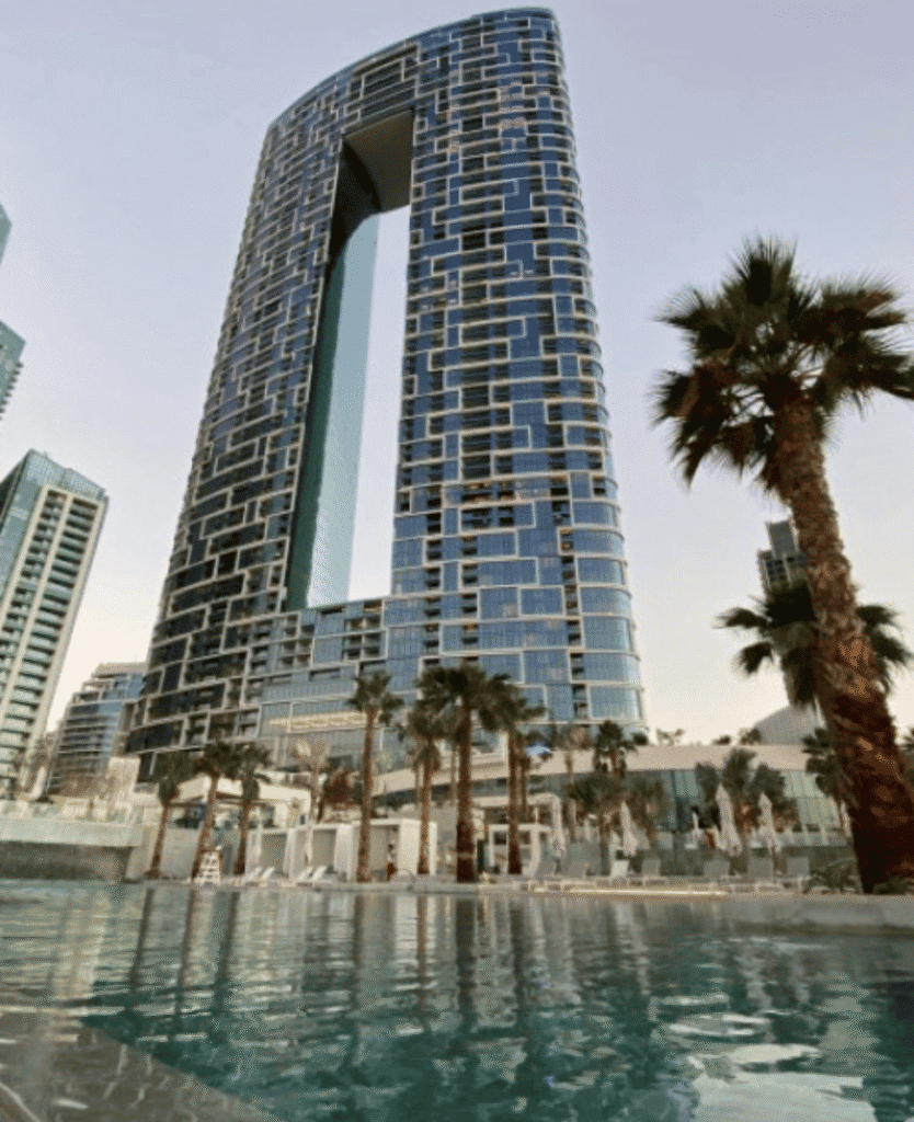 Luxury modern skyscraper with unique geometric design near palm trees in urban cityscape.