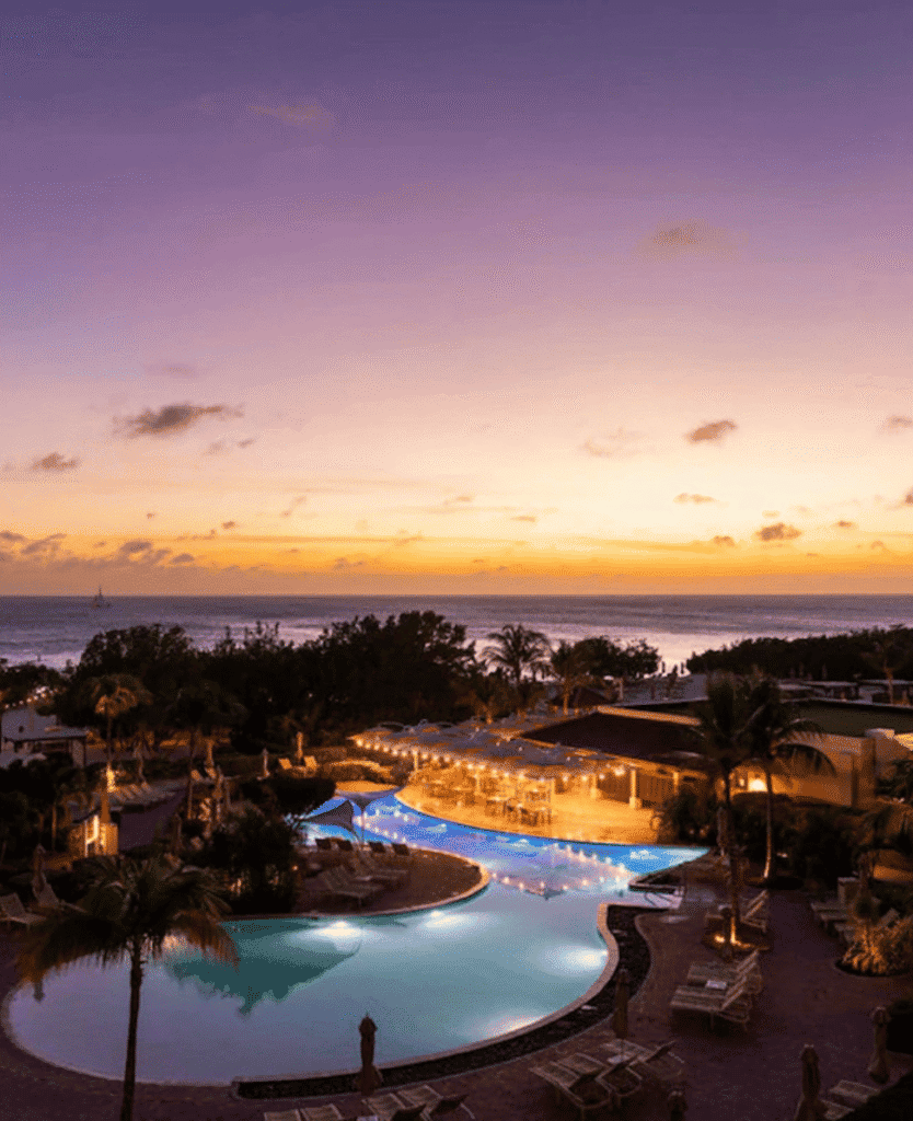 Sunset over luxurious beachside resort with swimming pool and tropical trees, evening relaxation.