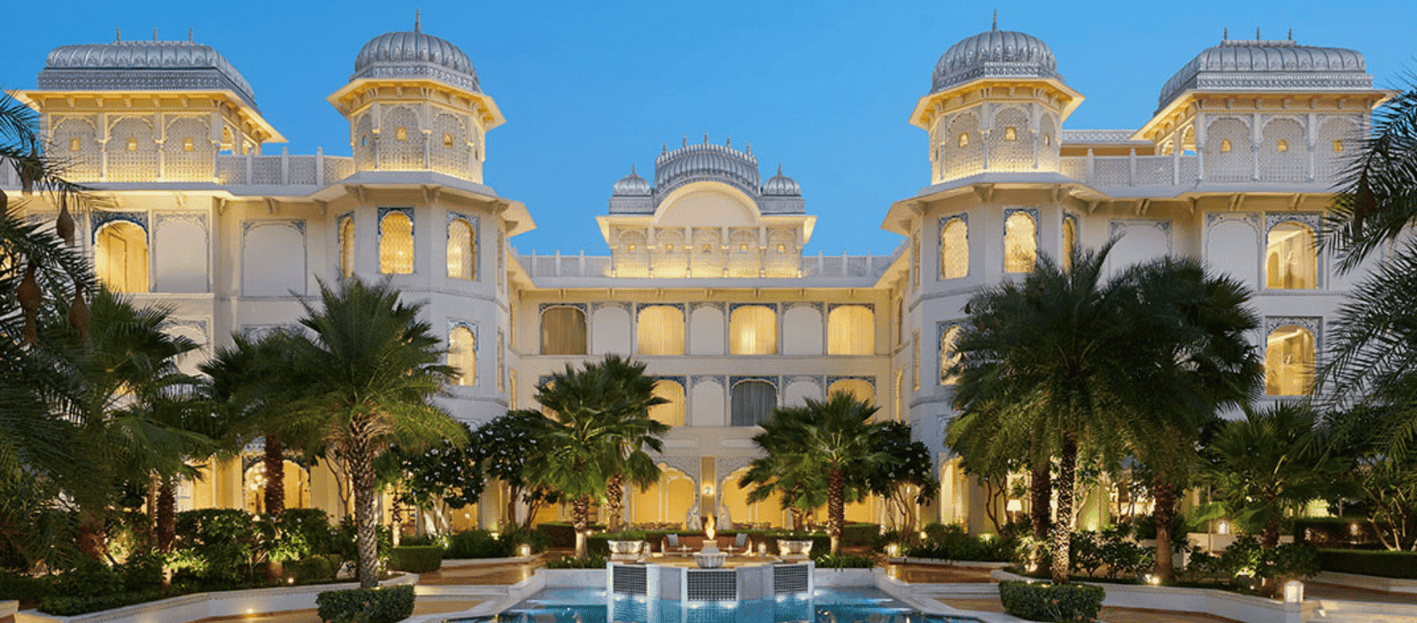 Luxurious white palace with elegant architecture and lush tropical landscaping at dusk.