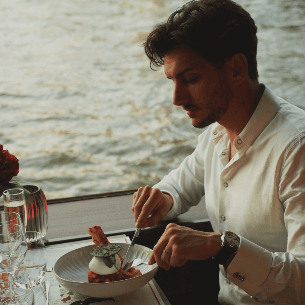 Luxury dining by the water, elegant man enjoying gourmet meal, sophisticated restaurant setting, scenic waterfront dining experience, fine dining on a boat with view.