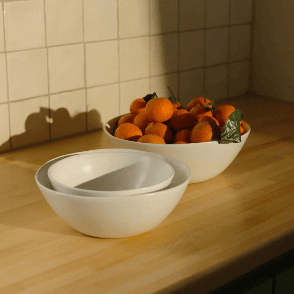 Fresh mandarin oranges in white ceramic bowls on a wooden kitchen counter.