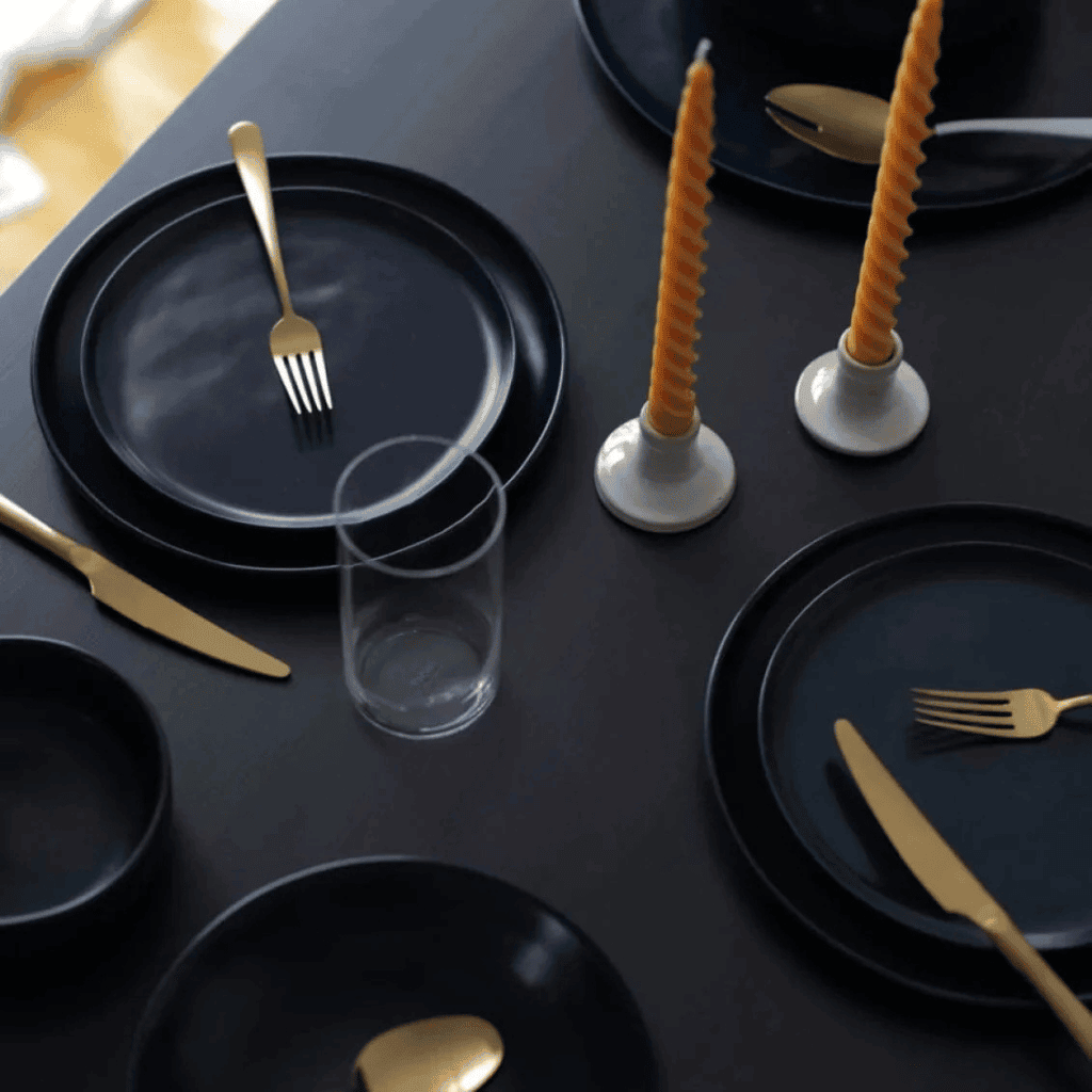 Elegant black dinnerware with gold cutlery and candles, perfect for stylish dining and table setting inspiration.