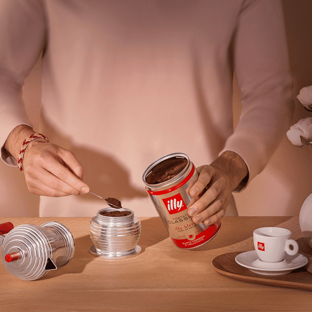 Illy coffee jar with spoon, latte practitioner, espresso set, and coffee cup on wooden table.