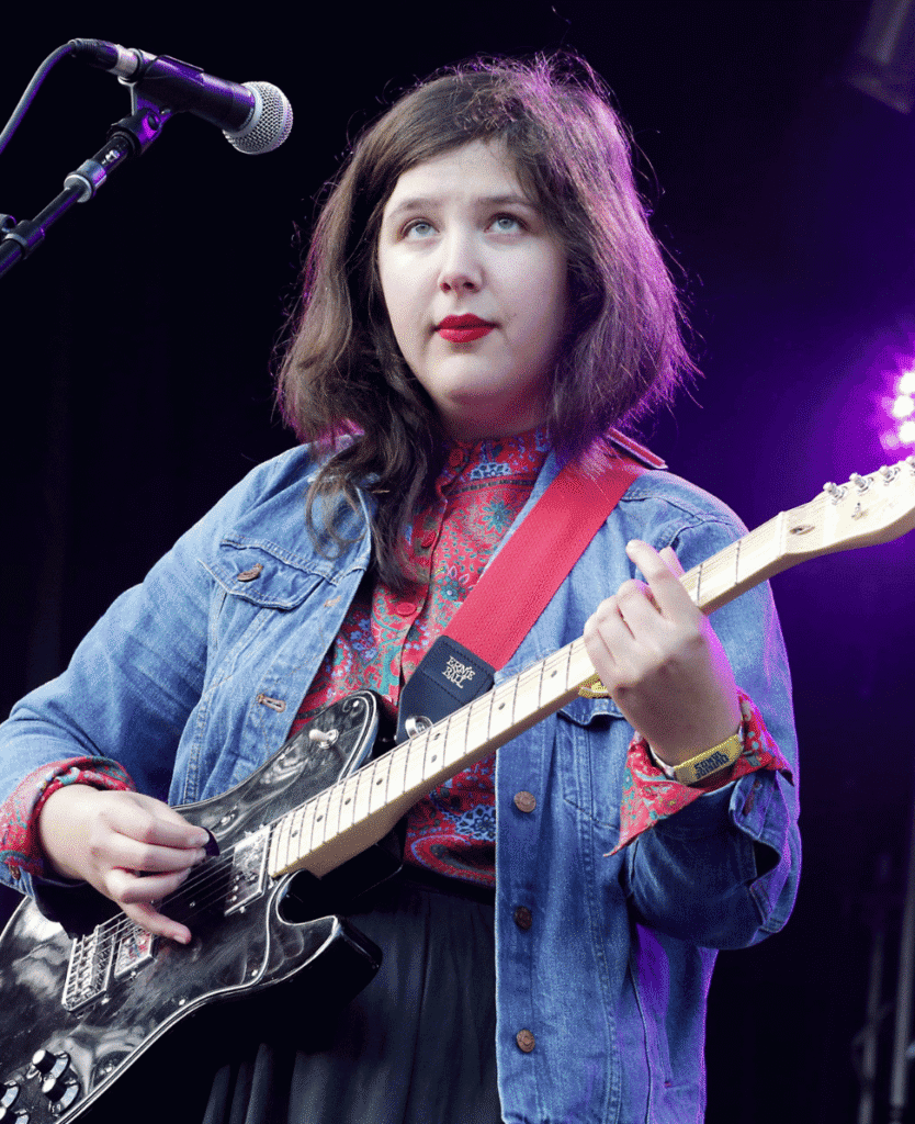 Girl playing electric guitar at live music concert, young female musician on stage with purple lighting.
