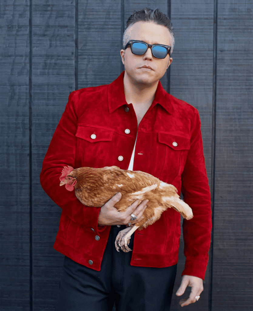 Chic man holding chicken, stylish fashion, urban background, trendy men's clothing, modern street style.