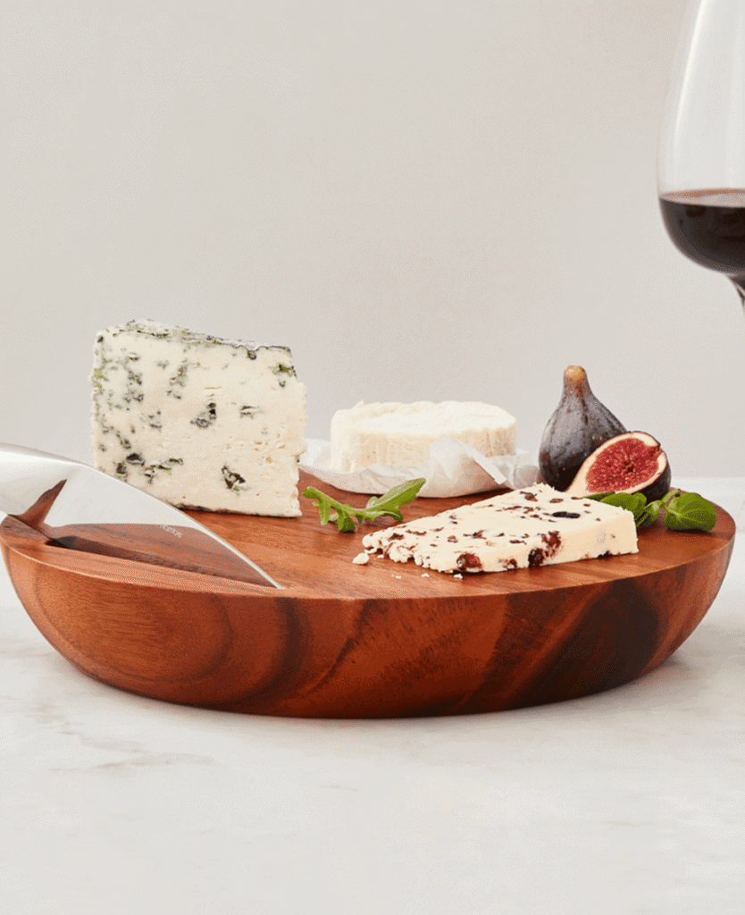 Cheese platter with blue cheese, brie, dried figs, fresh figs, and arugula on a wooden serving board.