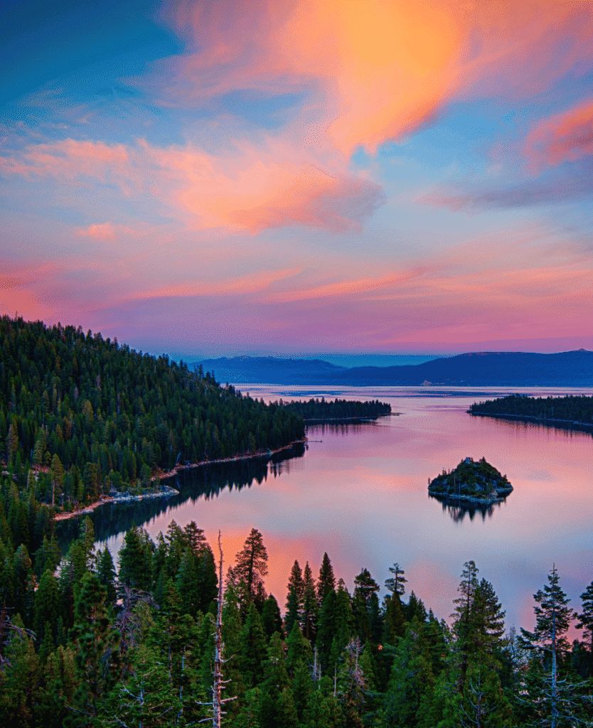Mountain lake at sunset with pink and blue sky and dense forest in foreground.