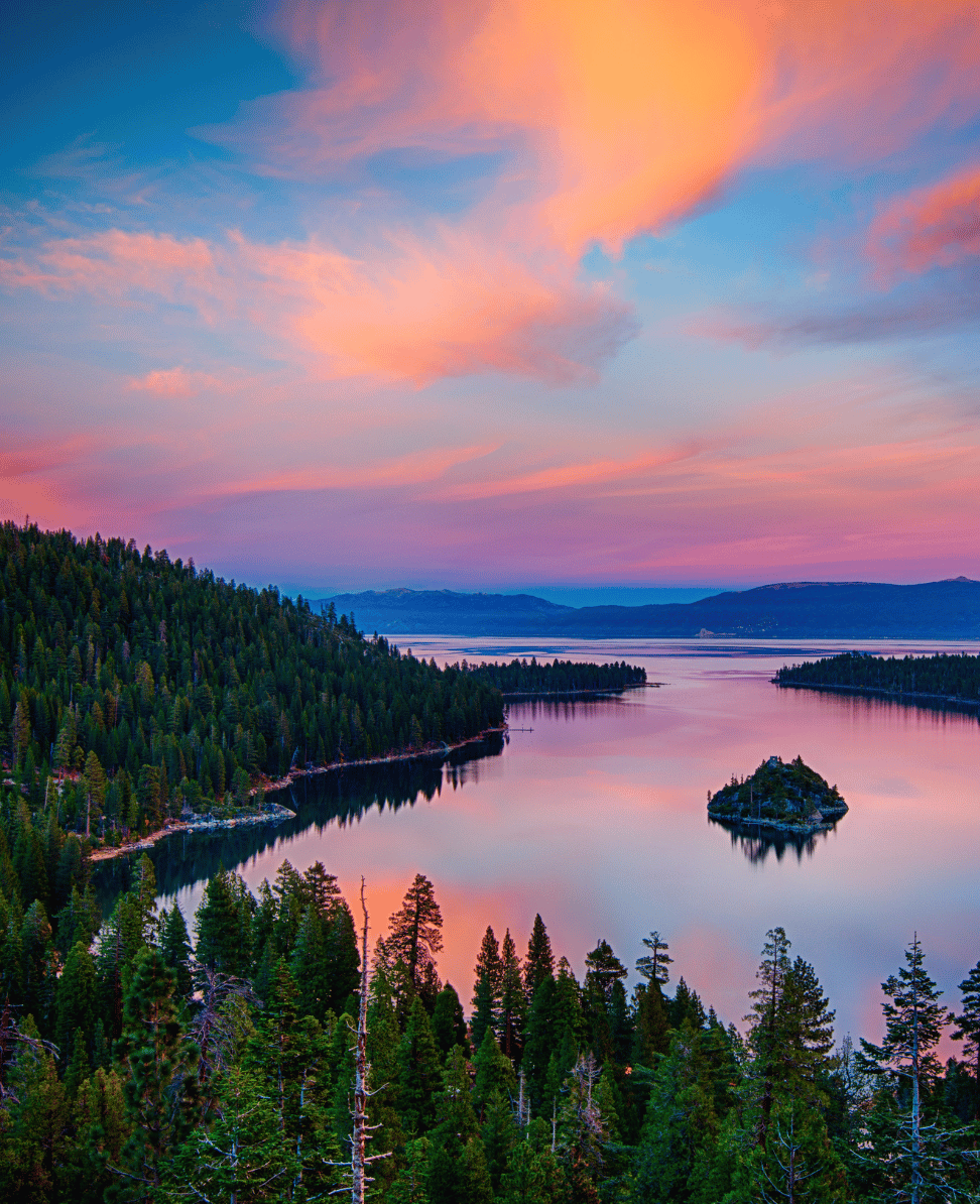 Mountain lake at sunset with pink and blue sky and dense forest in foreground.
