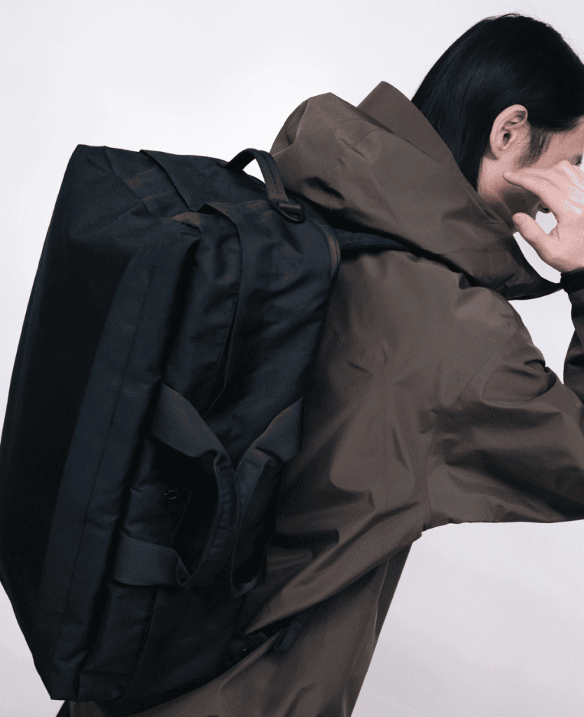 Travel backpack and outdoor gear, woman wearing brown jacket and black backpack, minimalist urban style, ready for adventure.