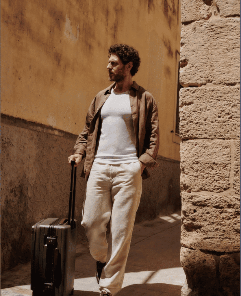 Traveling man with a suitcase by the street, casual style, warm sunlight.