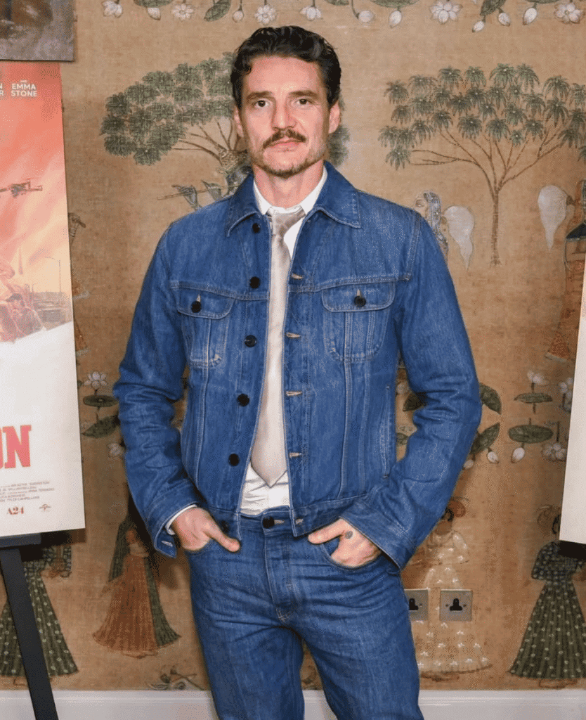 Denim jacket and jeans worn by a man standing in front of floral wallpaper.