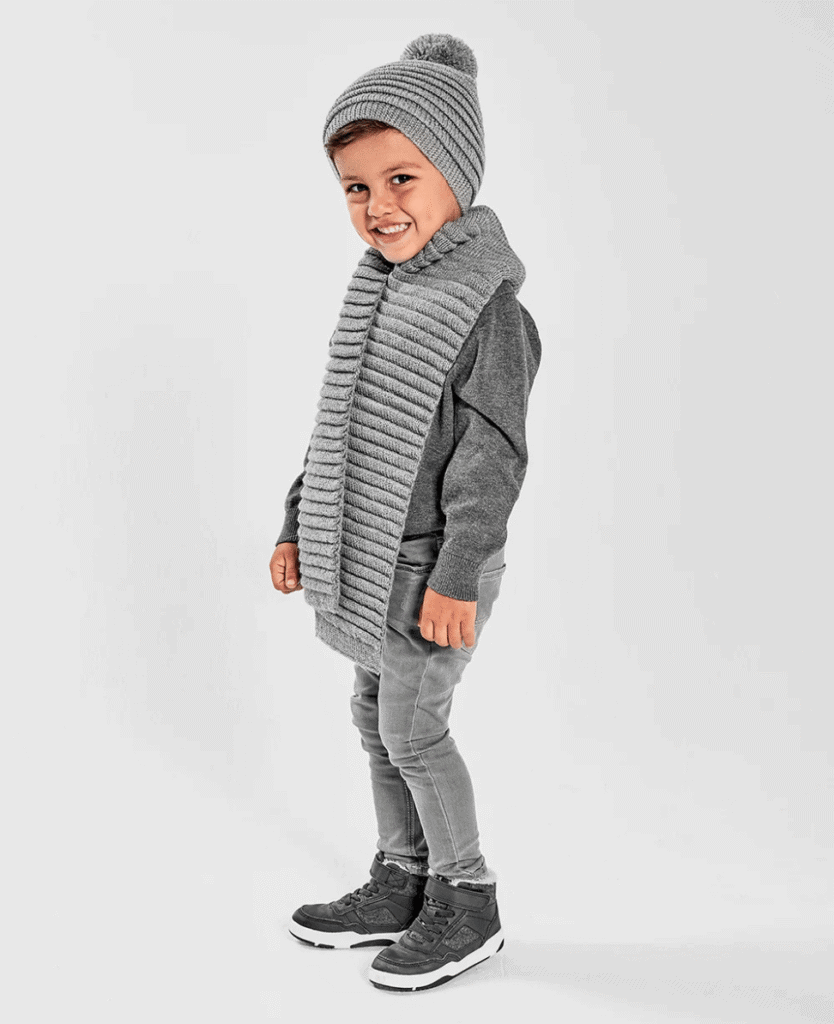 Warm children’s winter clothing, kids cozy knit hat, scarf, and winter boots for cold weather.