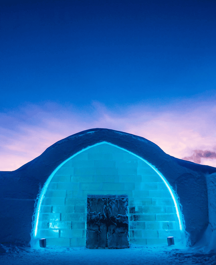 Igloo ice structure illuminated with blue neon lights at dusk, showcasing winter and travel adventure themes.