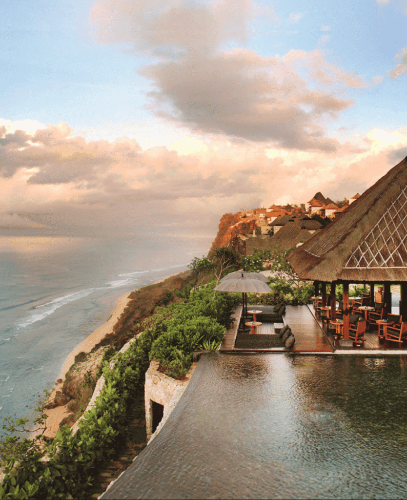 Seaside luxury resort with infinity pool overlooking the ocean at sunset, tropical greenery, and ocean view.