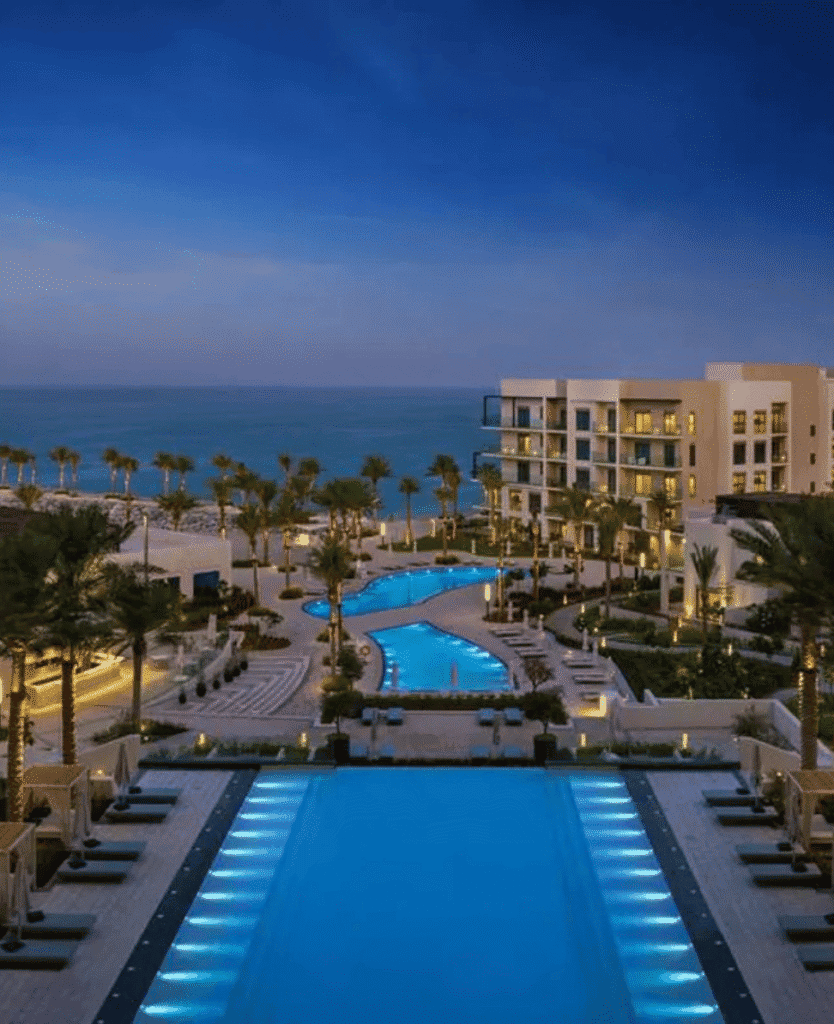 Luxury beachfront resort swimming pool at night, ocean view, palm trees, relaxing vacation destination, elegant hotel atmosphere.