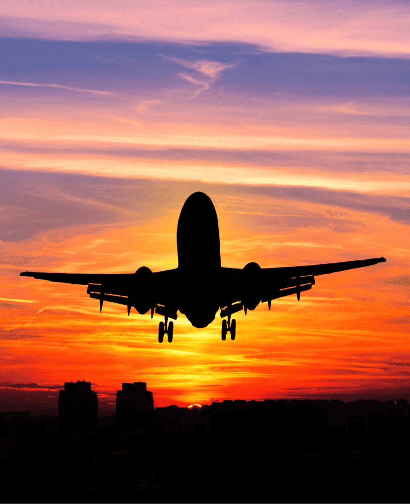 Airplane silhouette flying at sunset with vibrant colored sky.