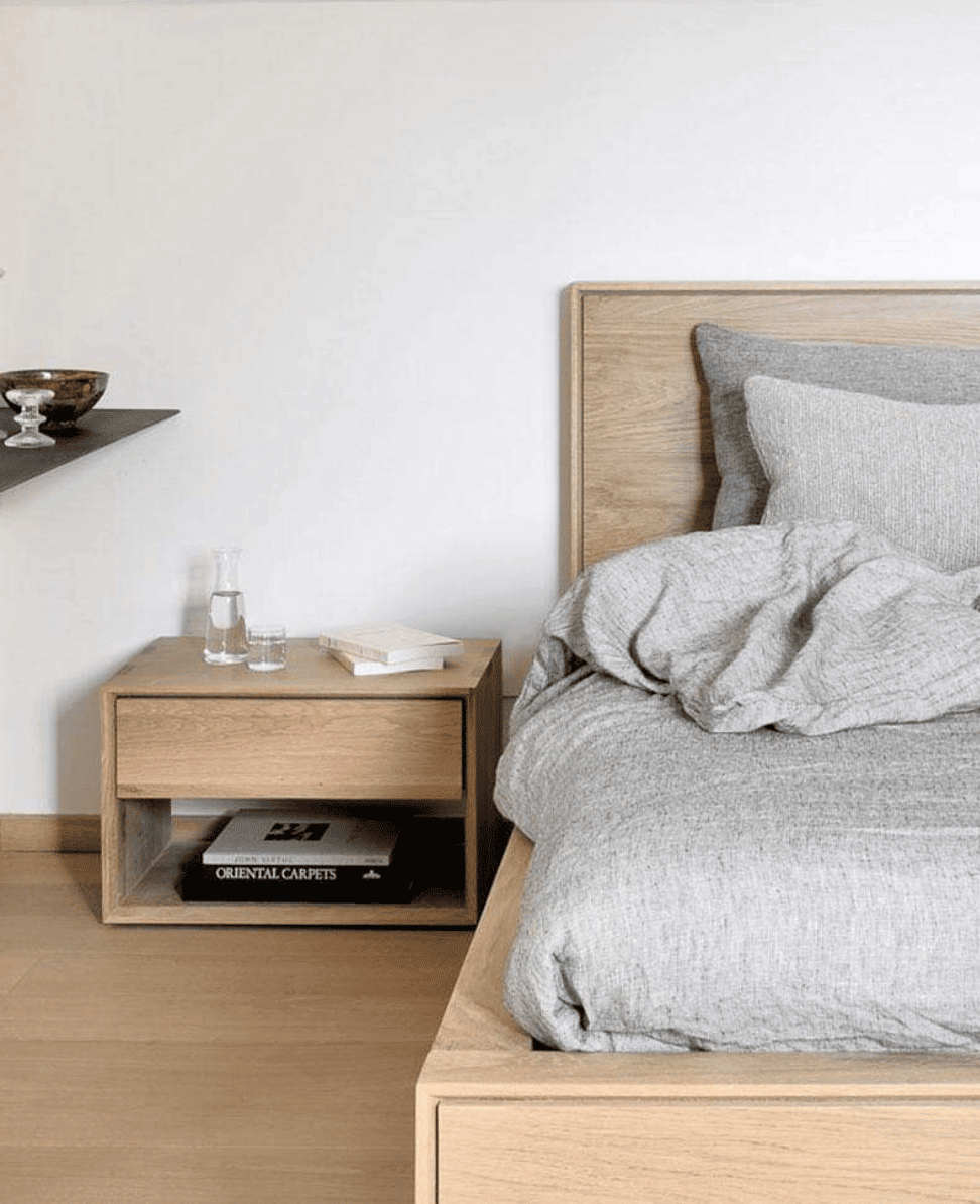 Cozy minimalist bedroom with wooden bed frame and nightstand, neutral-toned linens, modern decor, and natural light.