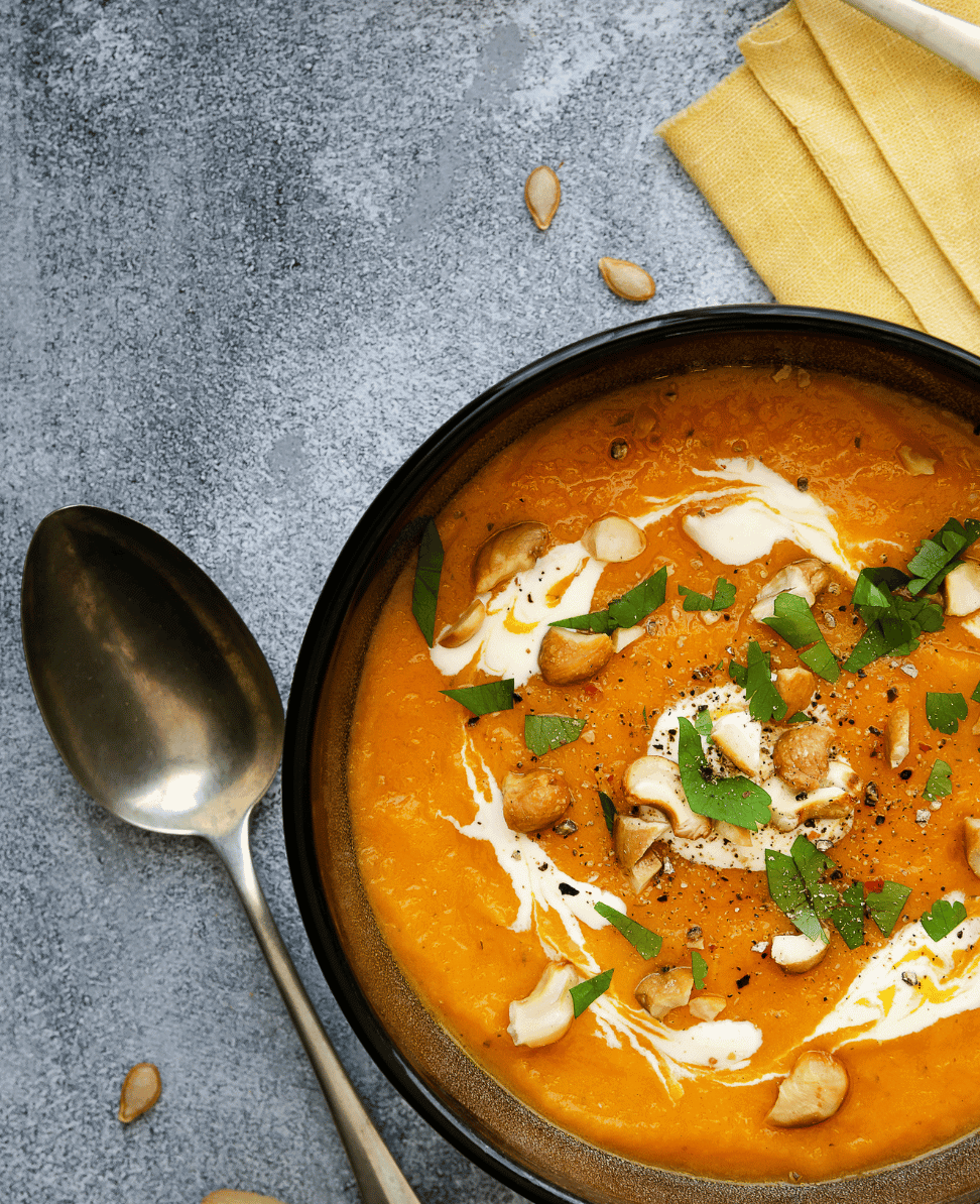 Creamy butternut squash soup garnished with cashews and herbs, served in a black bowl.