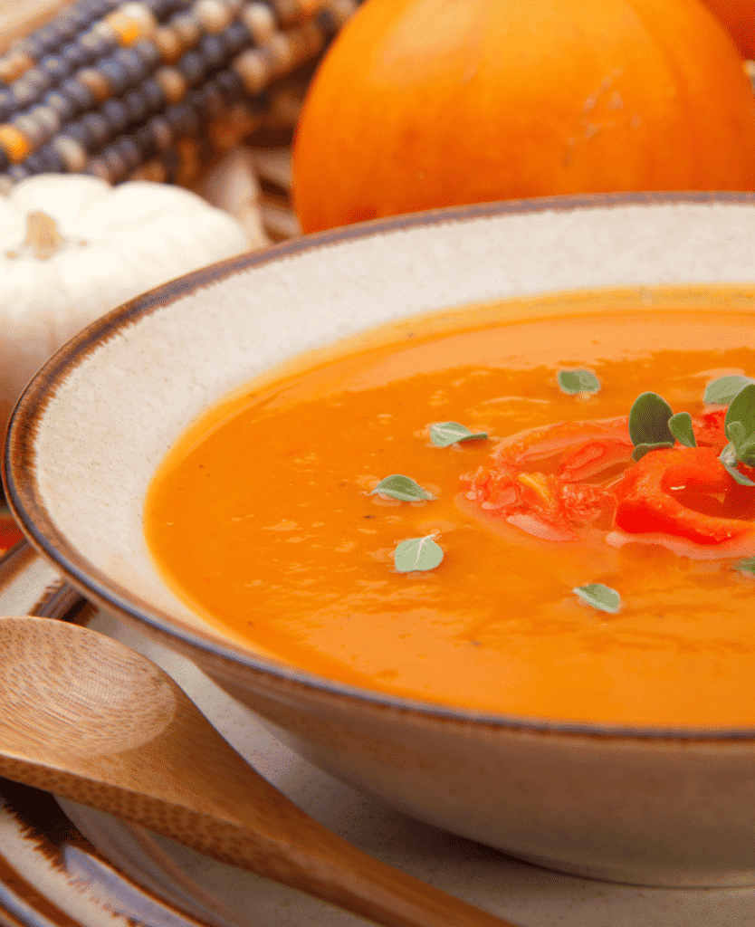 Bloody Mary tomato soup with fresh herbs, served in a rustic bowl, autumn-themed setting.