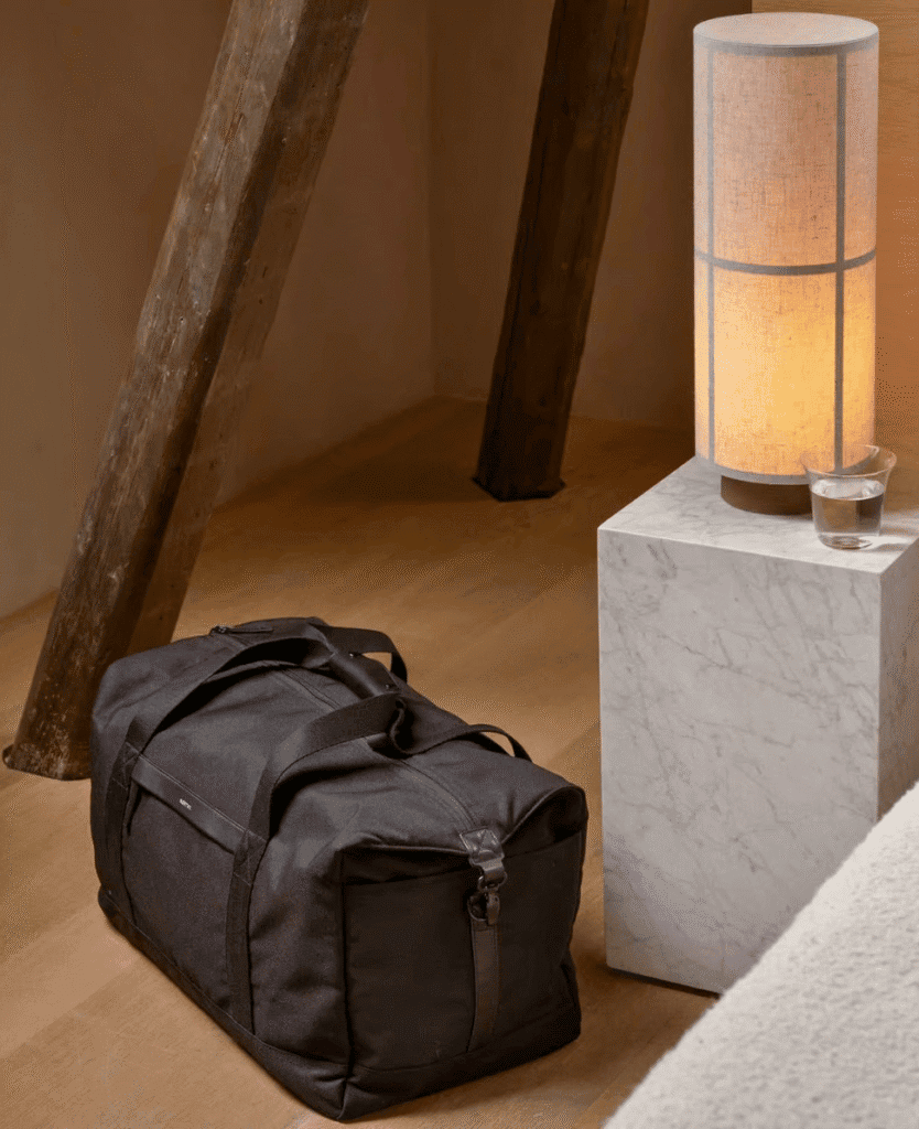 Travel duffel bag on wooden floor with modern lamp and marble side table.